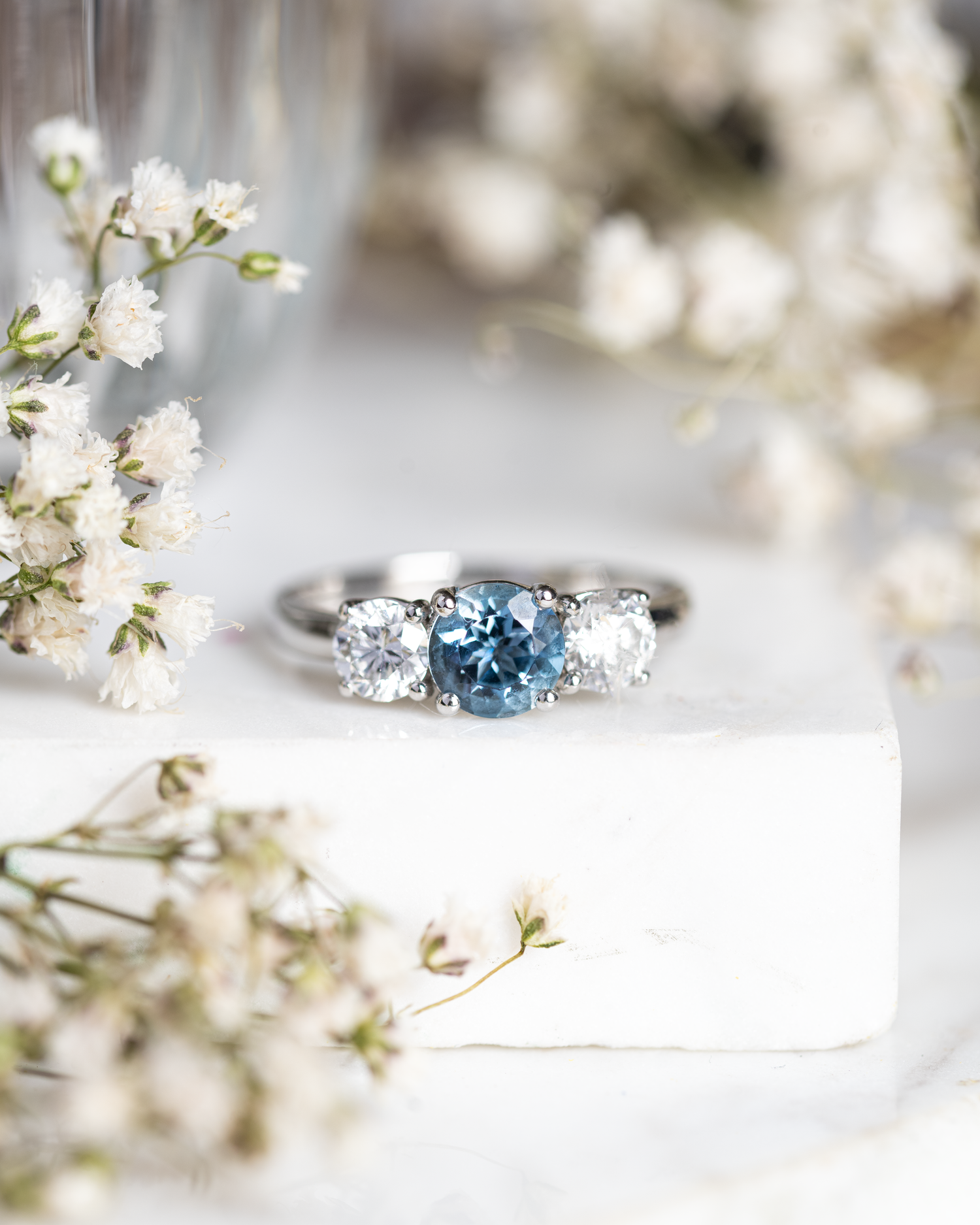 Aquamarine and Diamond Three Stone Ring photographed on a white marble base with flowers to compliment