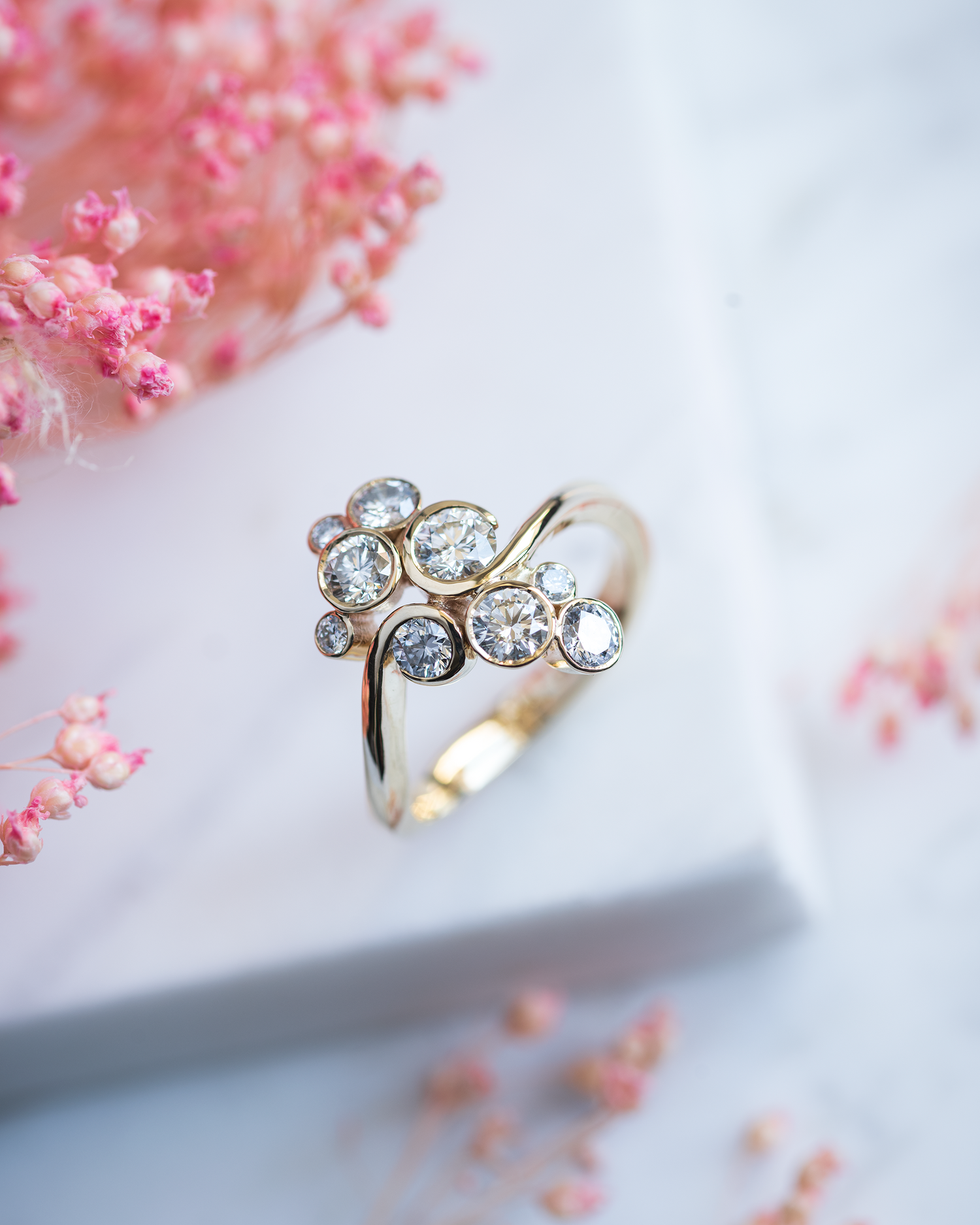 Contemporary Multi Stone Diamond Ring photographed on a grey marble base with pink flowers