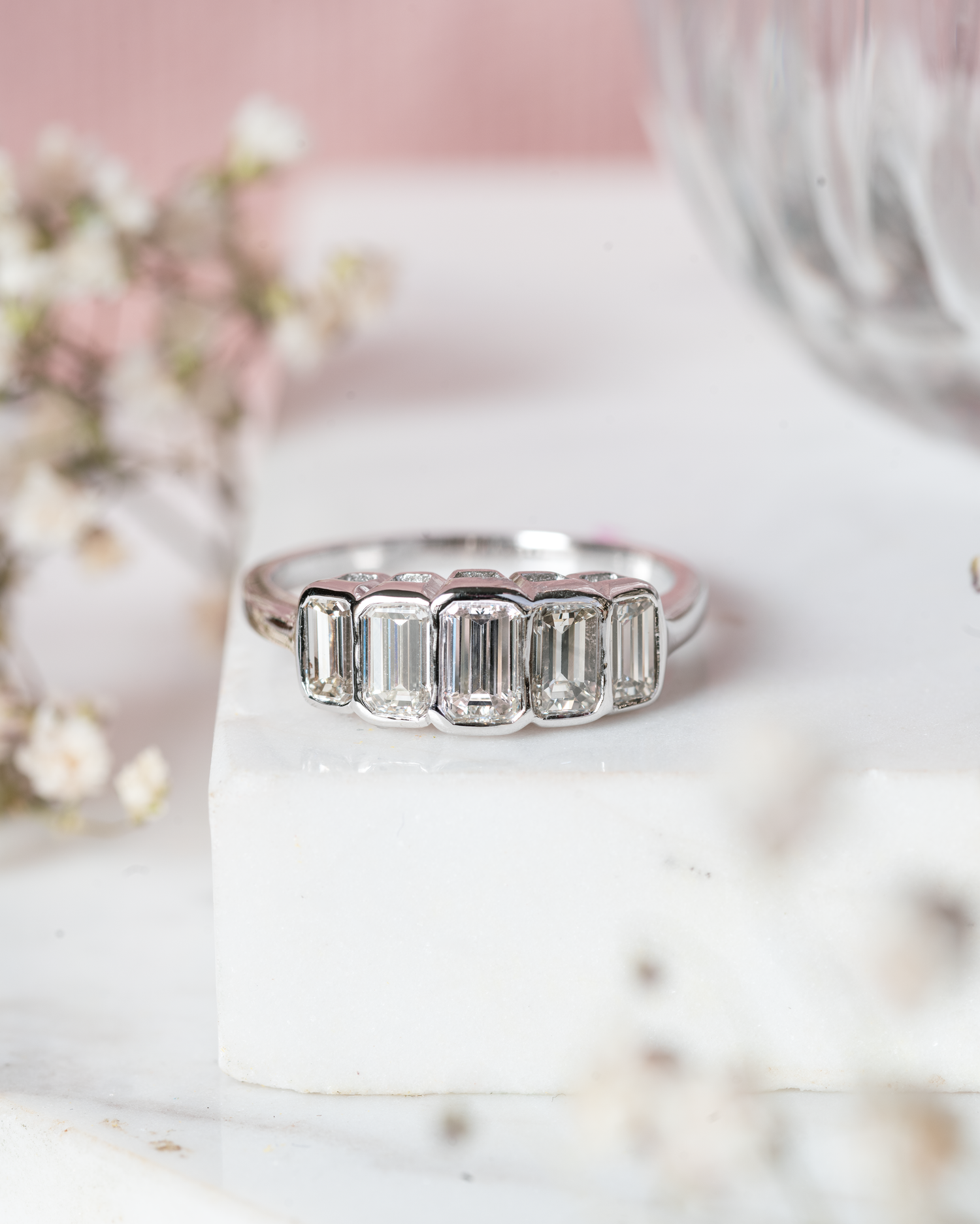 Emerald Cut Five Stone Diamond Ring photographed on marble base with floral accents