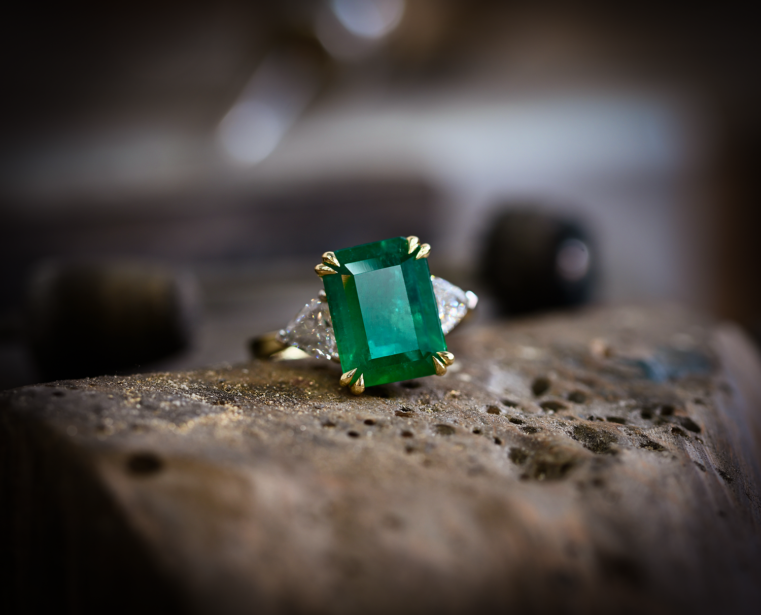 large emerald solitaire with double talon claw setting and trillion cut diamond shoulders. Photographed on a goldsmiths peg.