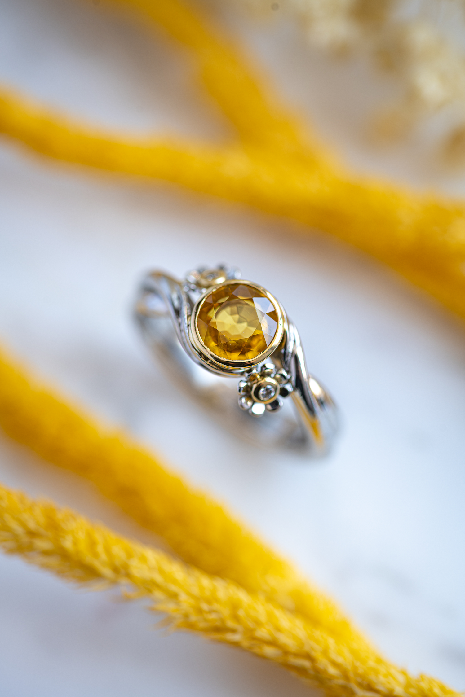 Yellow Sapphire and Diamond Flower Ring photographed on grey marble and accompanied with two sets of elongated yellow reeds