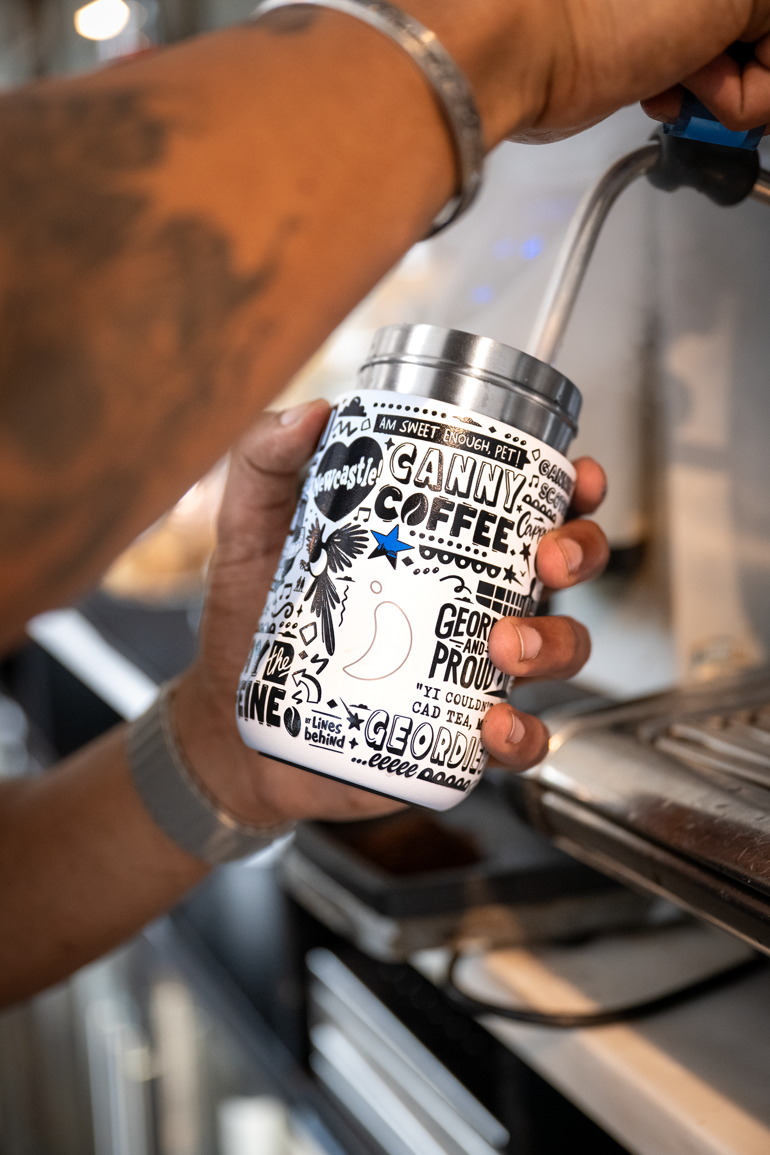 Person holding a branded coffee cup with a coffee machine in the background